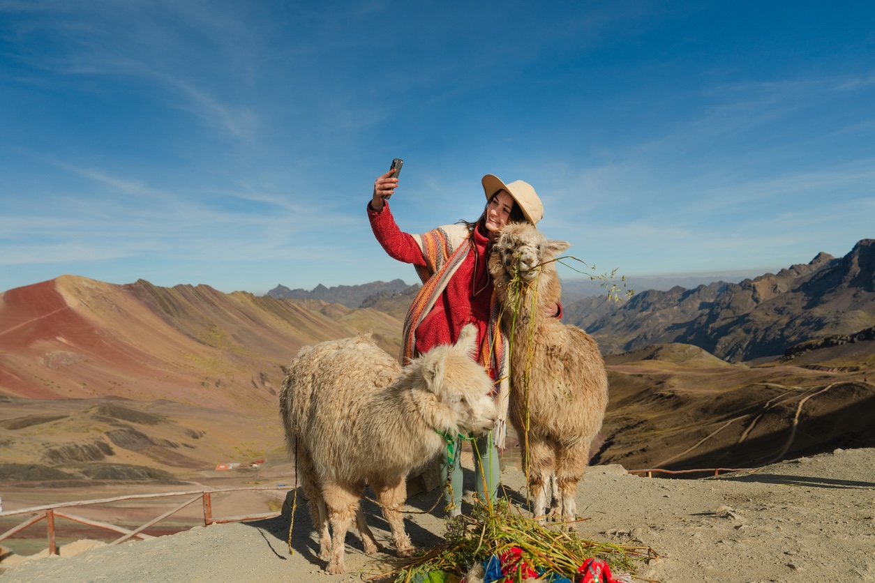 Cheerful woman with alpacas on the background of Rainbow mountain in Peru