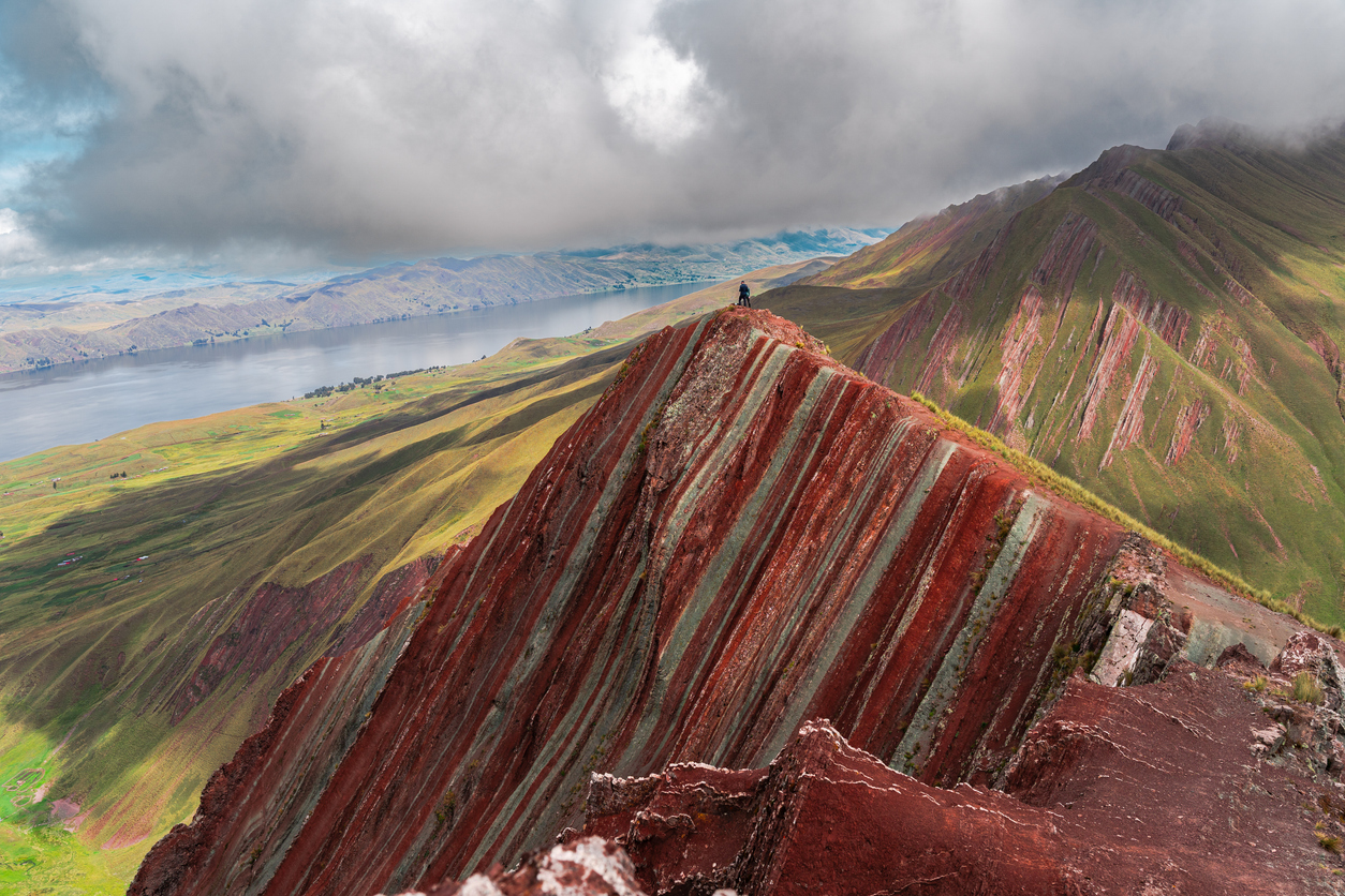 Person standing on Pallay Punchu colorful striped mountain ridge in Peruvian Andes