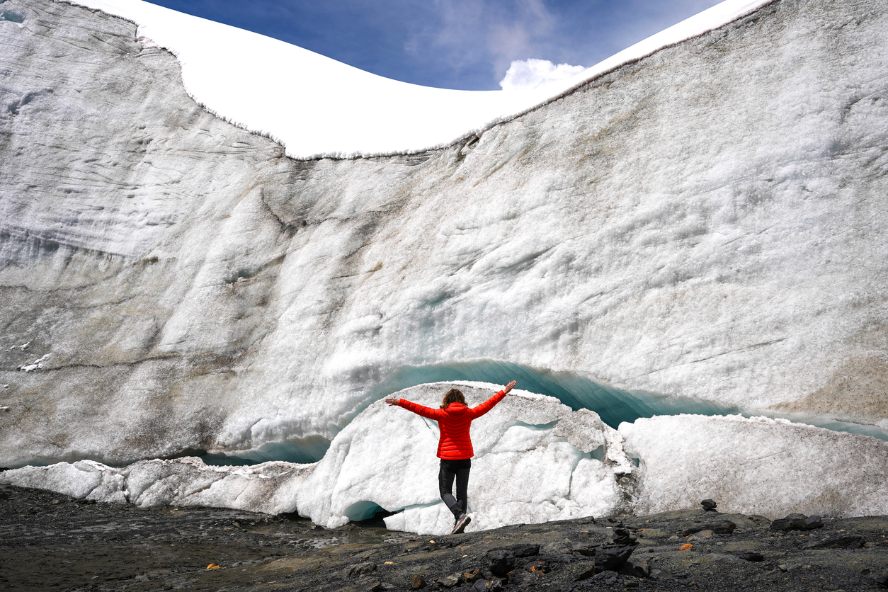 Hiker in red jacket celebrating success with arms raised on glacier in the Peruvian Andes