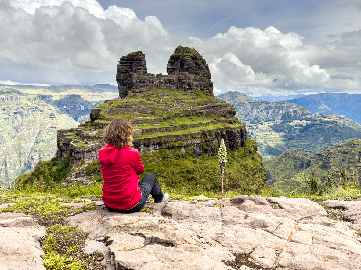 Woman traveler sitting overlooking Waqrapukara ruins in Peru